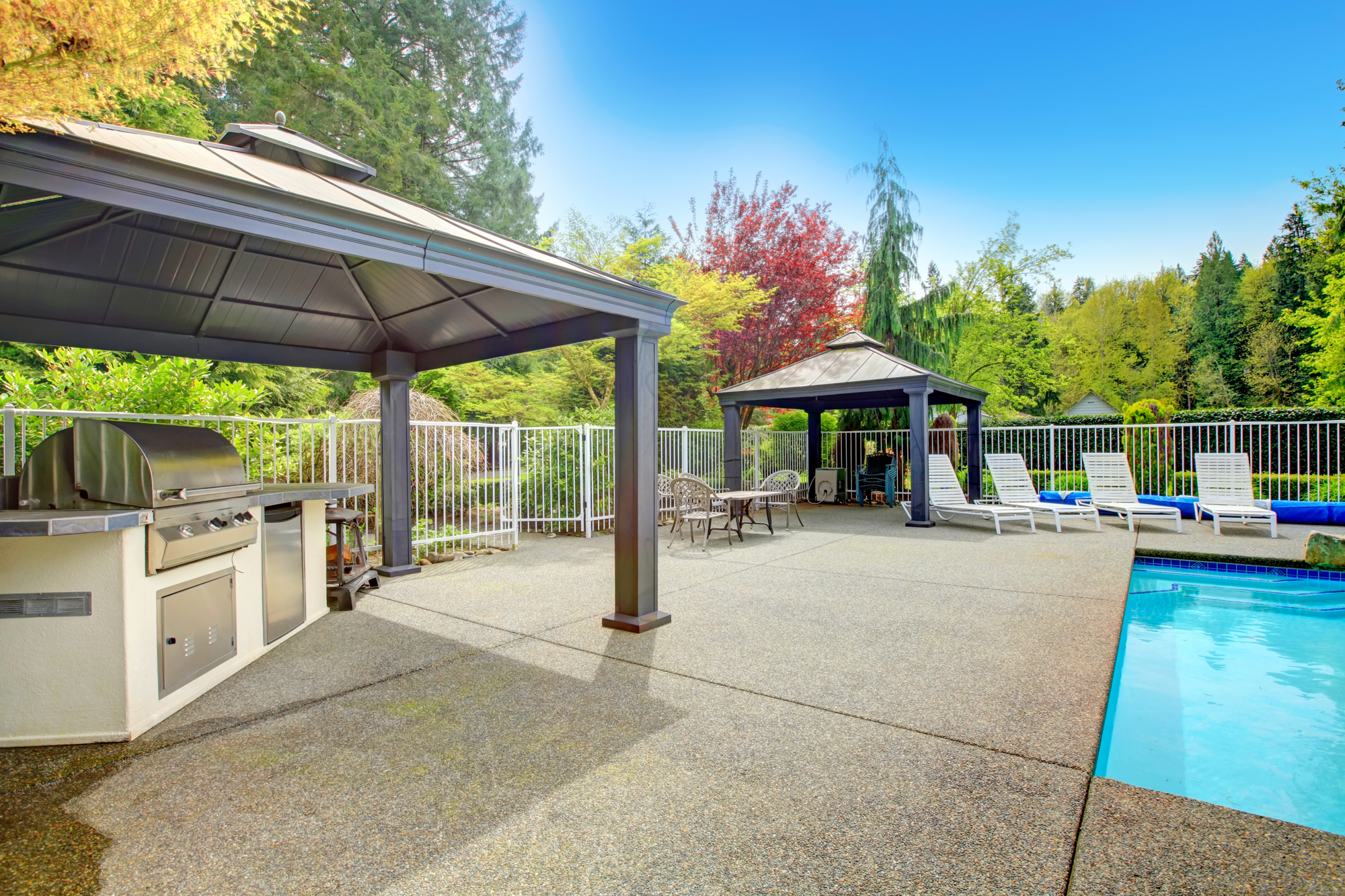 Concrete floor patio area with barbeque, table set, sun chairs and swimming pool